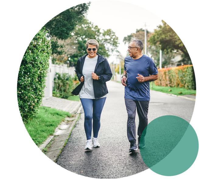 Hohes Cholesterin: Bewegungsmangel Eine Frau und ein Mann höheren Alters in Sportkleidung. Sie joggen gemeinsam auf einer Straße.