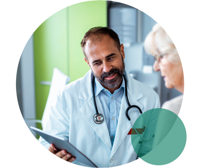Therapietreue bei Hypercholesterinämie Ein Arzt und eine Patientin im Seniorenalter. Der Arzt hält ein Tablet, auf das beide blicken.