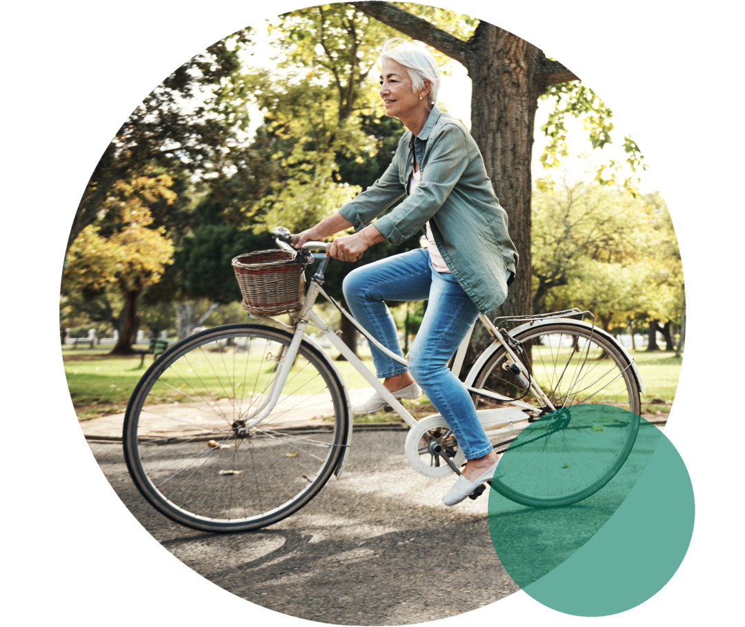 Cholesterin aktiv senken Eine Seniorin fährt in einem Park auf einem Fahrrad.