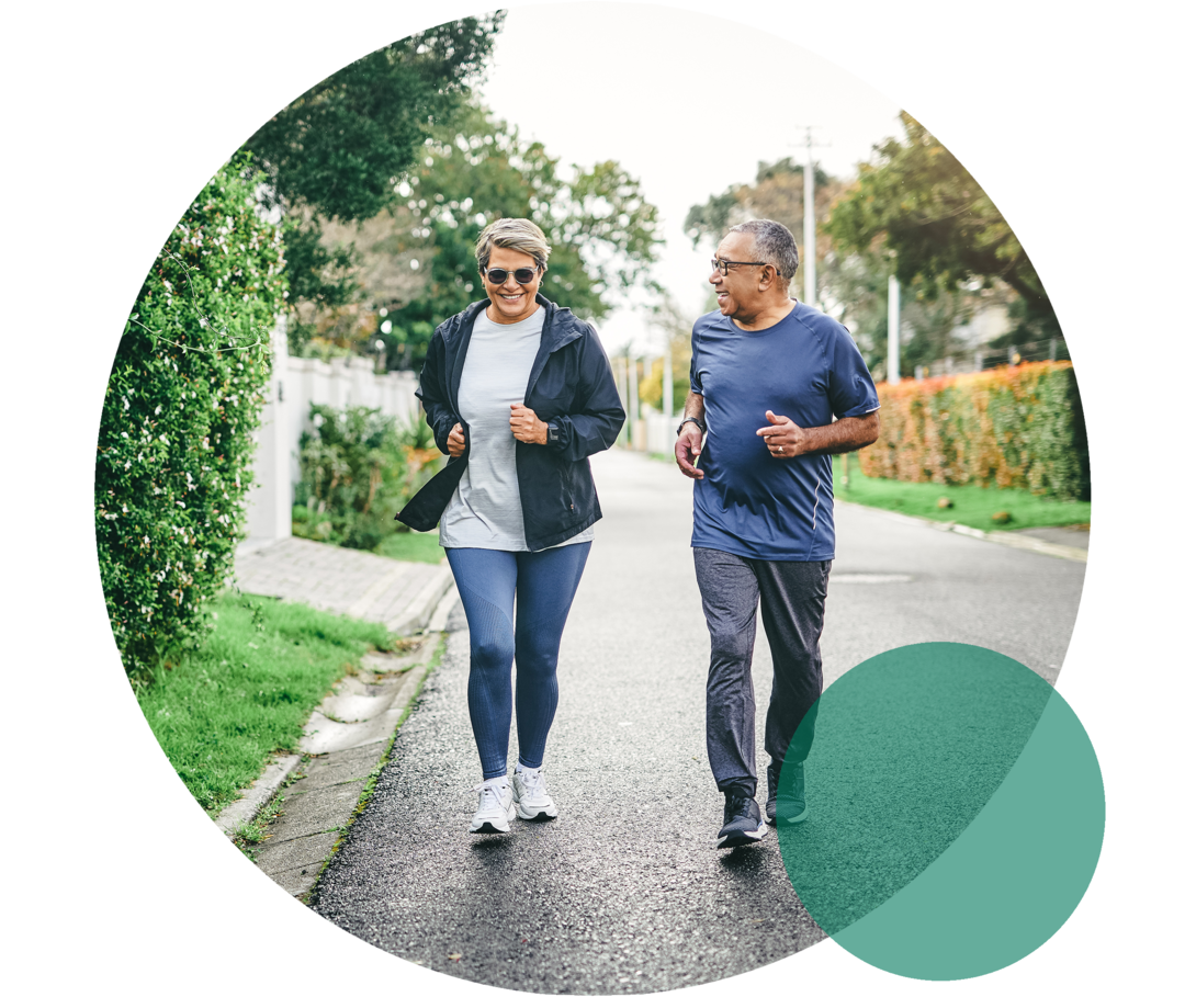 Hohes Cholesterin: Bewegungsmangel Eine Frau und ein Mann höheren Alters in Sportkleidung. Sie joggen gemeinsam auf einer Straße.