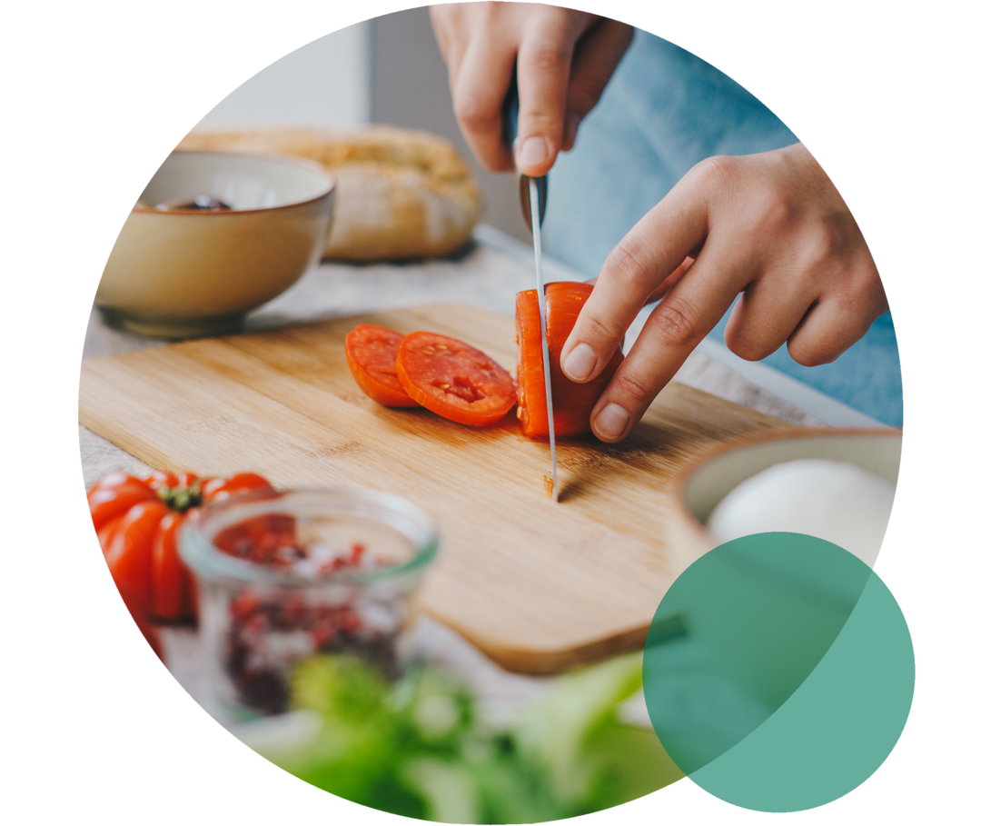 Ernährung bei Hypercholesterinämie Küchenbrett auf einer Arbeitsplatte. Zwei Hände schneiden eine Tomate mit einem Messer.