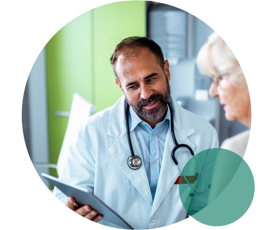 Therapietreue bei Hypercholesterinämie Ein Arzt und eine Patientin im Seniorenalter. Der Arzt hält ein Tablet, auf das beide blicken.