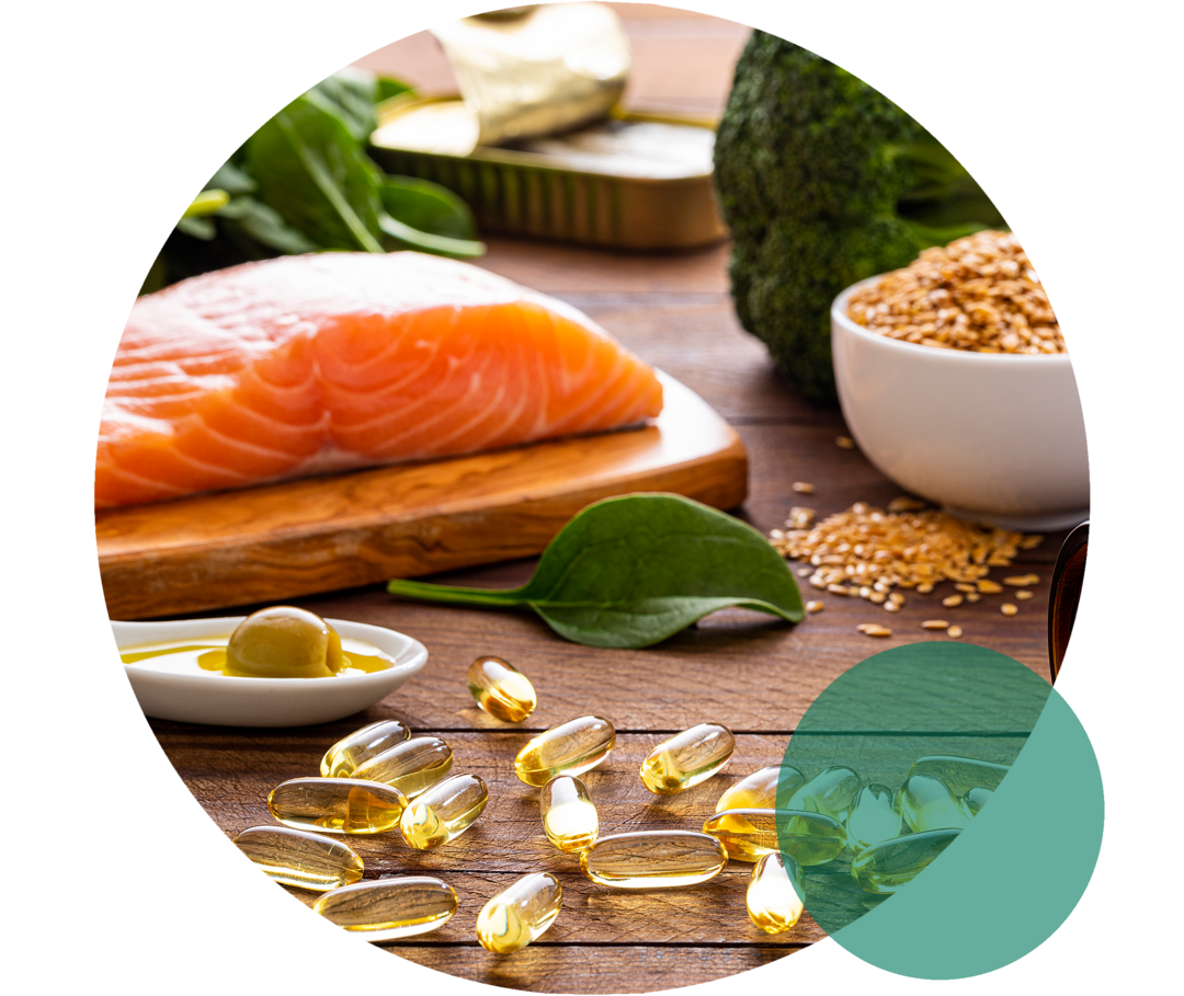 Erhöhte Triglyceride: Gesunde Ernährung mit Omega-3-Fettsäuren Auf einer Fläche liegen Lachs, Blattspinat, Brokkoli, ein Löffel mit Olivenöl sowie gelbliche Kapseln.